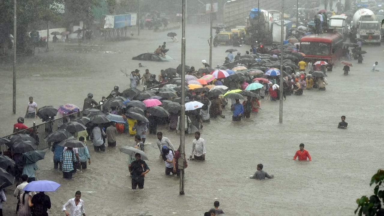 Menschen waten imm indischen Mumbai über eine überflutete Straße.