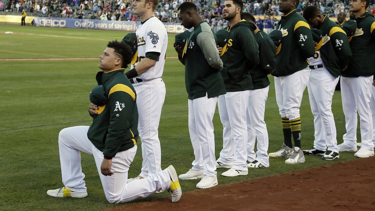 Der US-amerikanische Baseball-Spieler Bruce Maxwell (l) kniet in Oakland während der US-Nationalhymne.