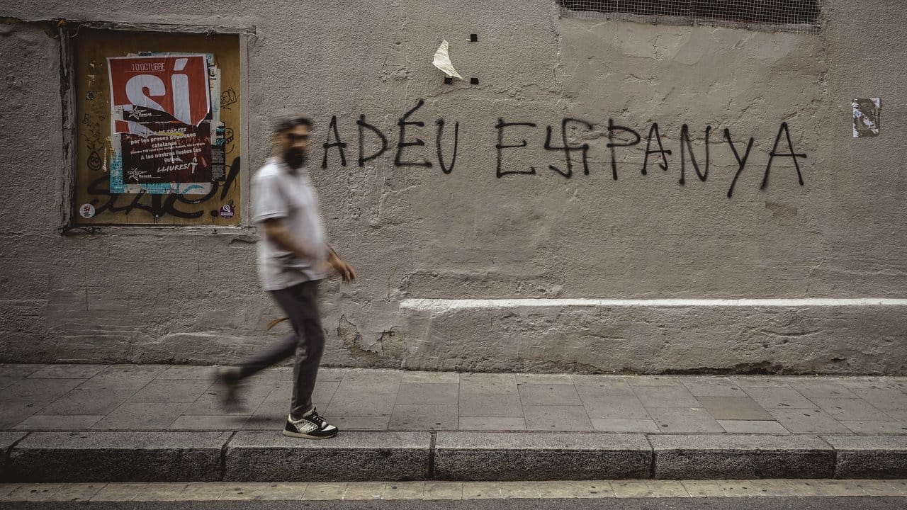 Ein Mann geht in Barcelona an einer Mauer vorbei, auf der auf Katalansich "Auf Wiedersehen Spanien" steht. Ein Mann geht in Barcelona an einer Mauer vorbei, auf der auf Katalansich "Auf Wiedersehen Spanien" steht.