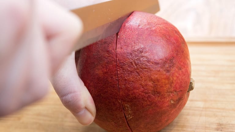 Ein Sägemesser vorsichtig ansetzen und den Granatapfel ein paar Millimeter rundherum einschneiden.