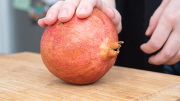 Den Granatapfel auf ein Küchenbrett legen und mit der Handfläche hin- und herrollen, dabei die Schale leicht eindrücken.
