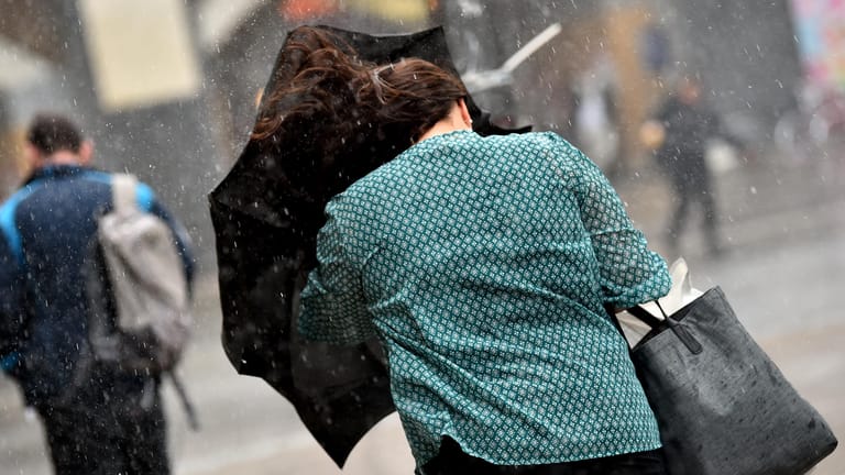 Eine junge Frauen kämpft in Berlin bei Starkwind mit einem Regenschirm.
