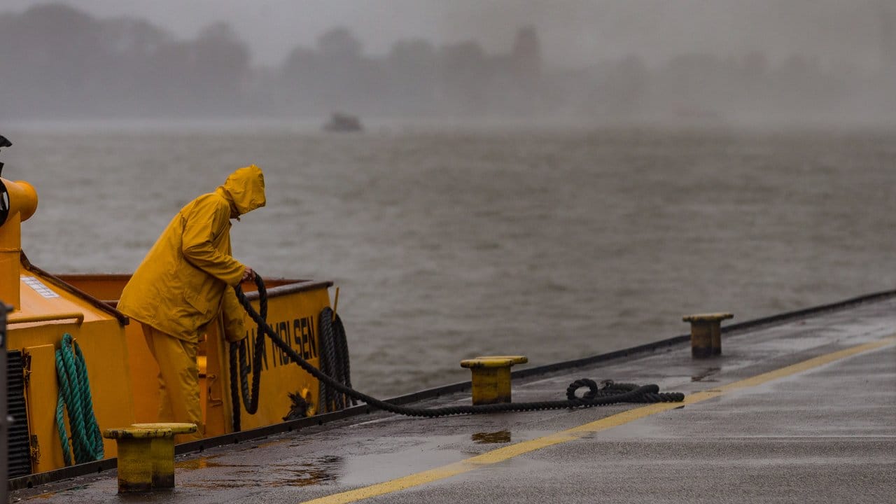 Bei trübem Regenwetter macht ein Matrose im Hafen in Hamburg die Leinen los.