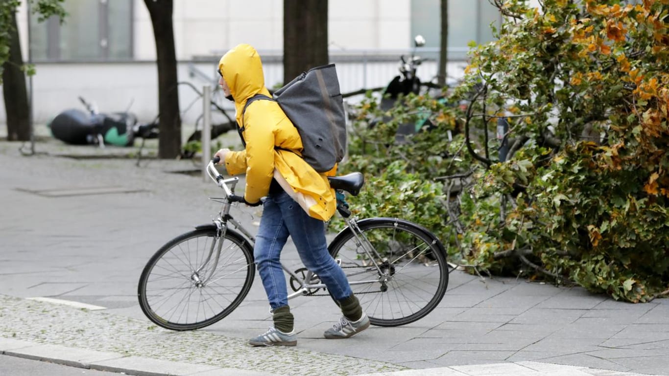 Eine Frau schiebt ihr Fahrrad in Berlin während des Sturms "Xavier" an einem herabgestürzten Ast vorbei.