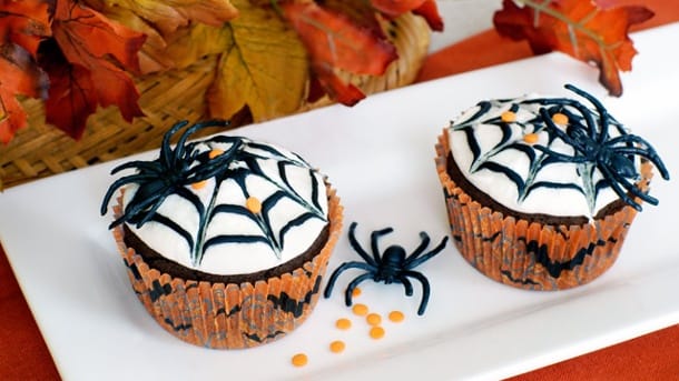 Halloween-Muffins mit weißer Glasur und aufgemalten Spinnenweben und Spinnen.
