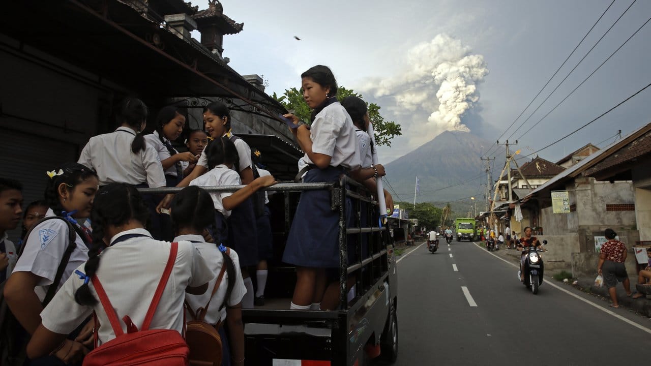 Auf dem Weg zur Schule: Balinesische Jugendliche klettern auf einen Pick-up, während der Mount Agung im Hintergrund Rauch und Asche spuckt.