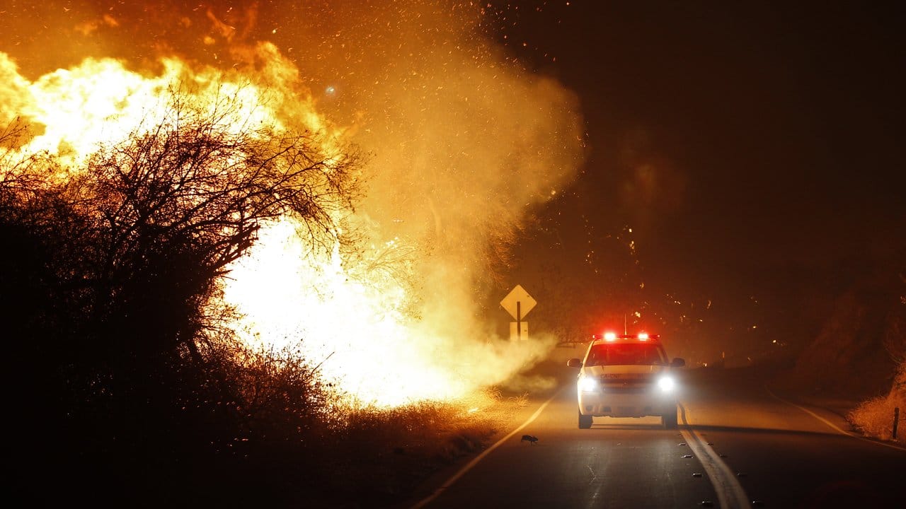 Unmittelbar neben brennendem Buschwerk rast ein Wagen der Feuerwehr unweit von San Diego zu seinem Einsatzort. Unmittelbar neben brennendem Buschwerk rast ein Wagen der Feuerwehr unweit von San Diego zu seinem Einsatzort.