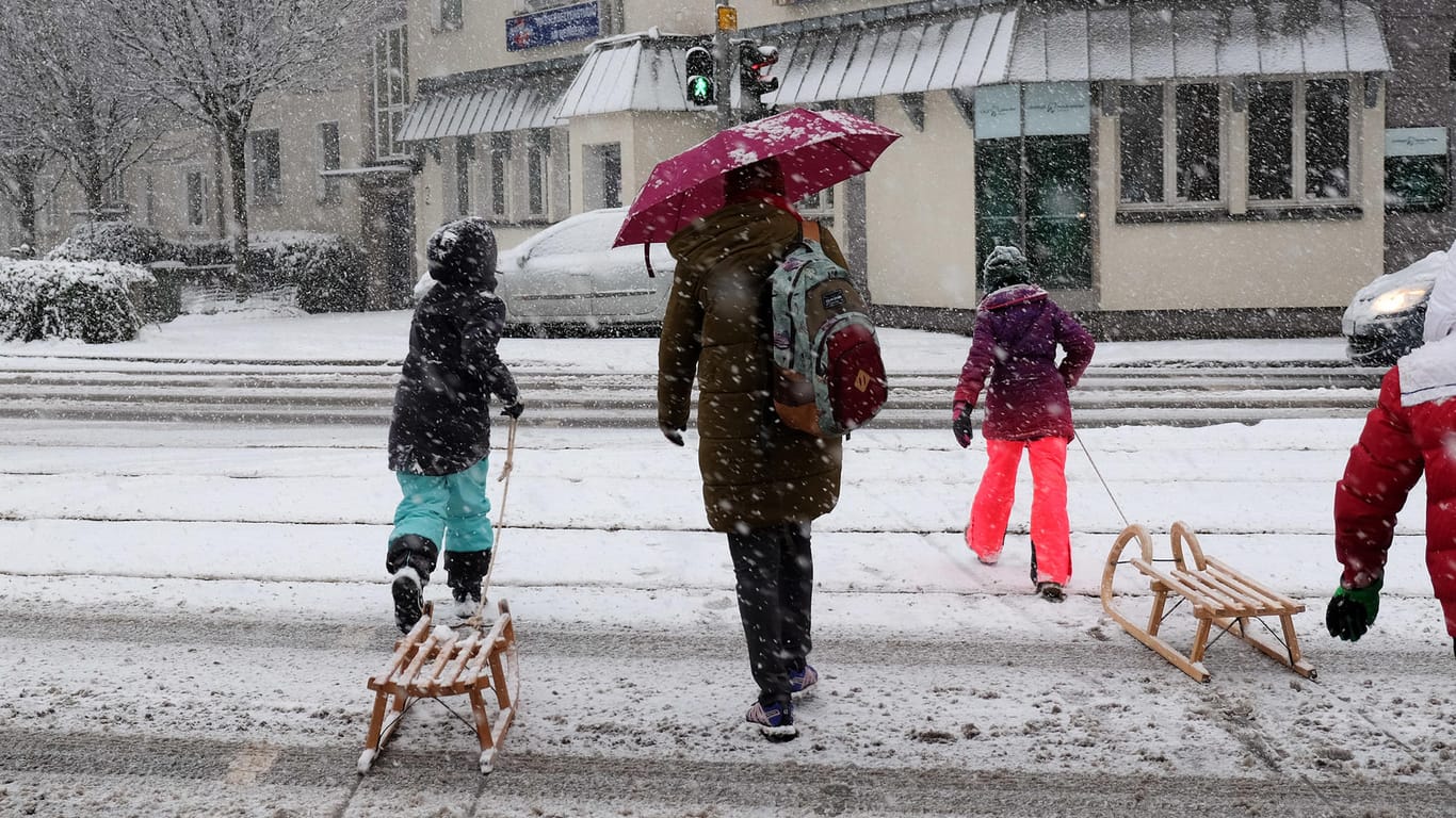 Kinder mit Schlitten überqueren in Kassel (Hessen) bei Schneefall eine Kreuzung.