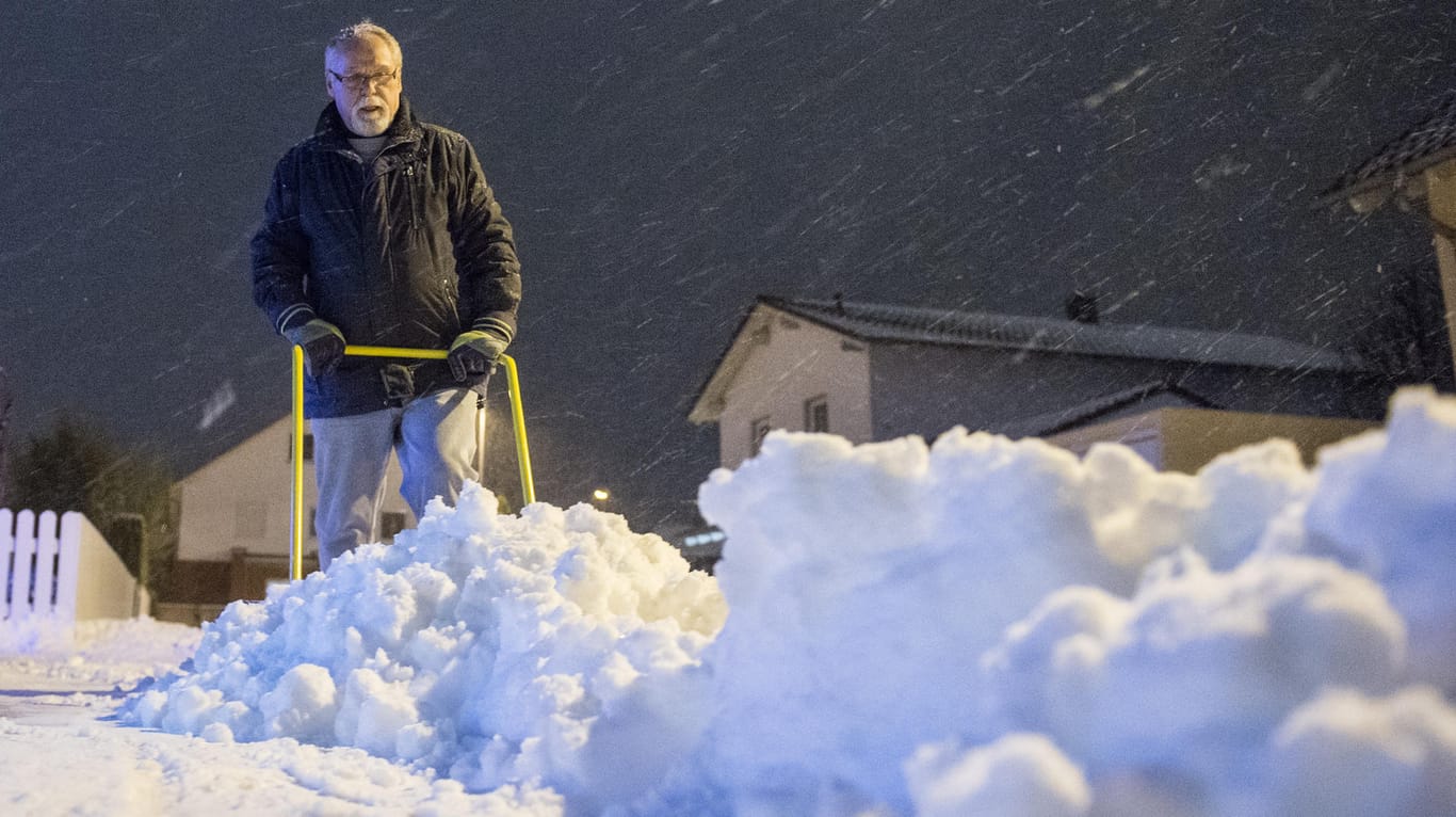 Ein Mann schaufelt im Abendlicht in Straubing (Bayern) Schnee vom Gehsteig.