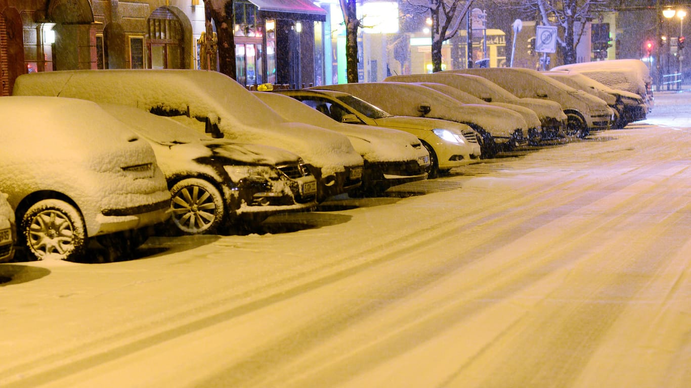 Schnee liegt in Berlin auf geparkten Autos und der Fahrbahn.
