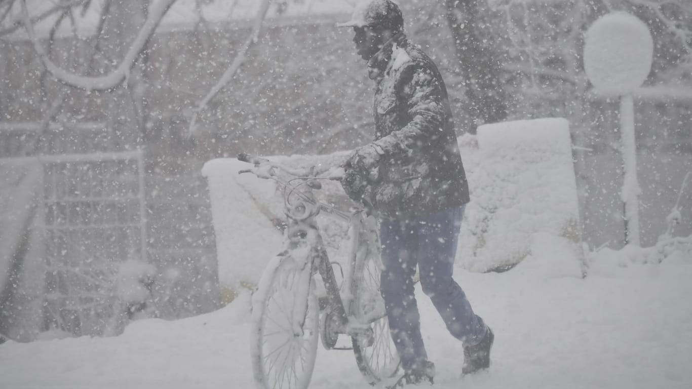 Ein Mann schiebt sein Fahrrad bei starkem Schneefall über eine schneebedeckte Straße in Antwerpen (Belgien).