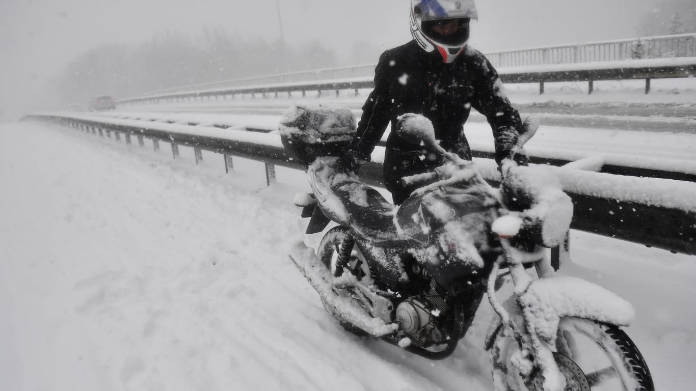 Ein Mann schiebt sein schneebedecktes Motorrad bei heftigem Schneetreiben am Rand der Autobahn E19 bei Kontich (Belgien) entlang