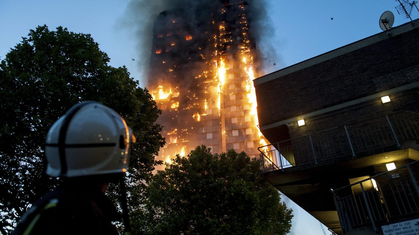 Feuerwehrleute beobachten hilflos, wie der Grenfell Tower in London abbrennt. Der Hochhausbrand steht beispielhaft für die Folgen von Sparwut und mangelhafte gesetzliche Vorschriften.