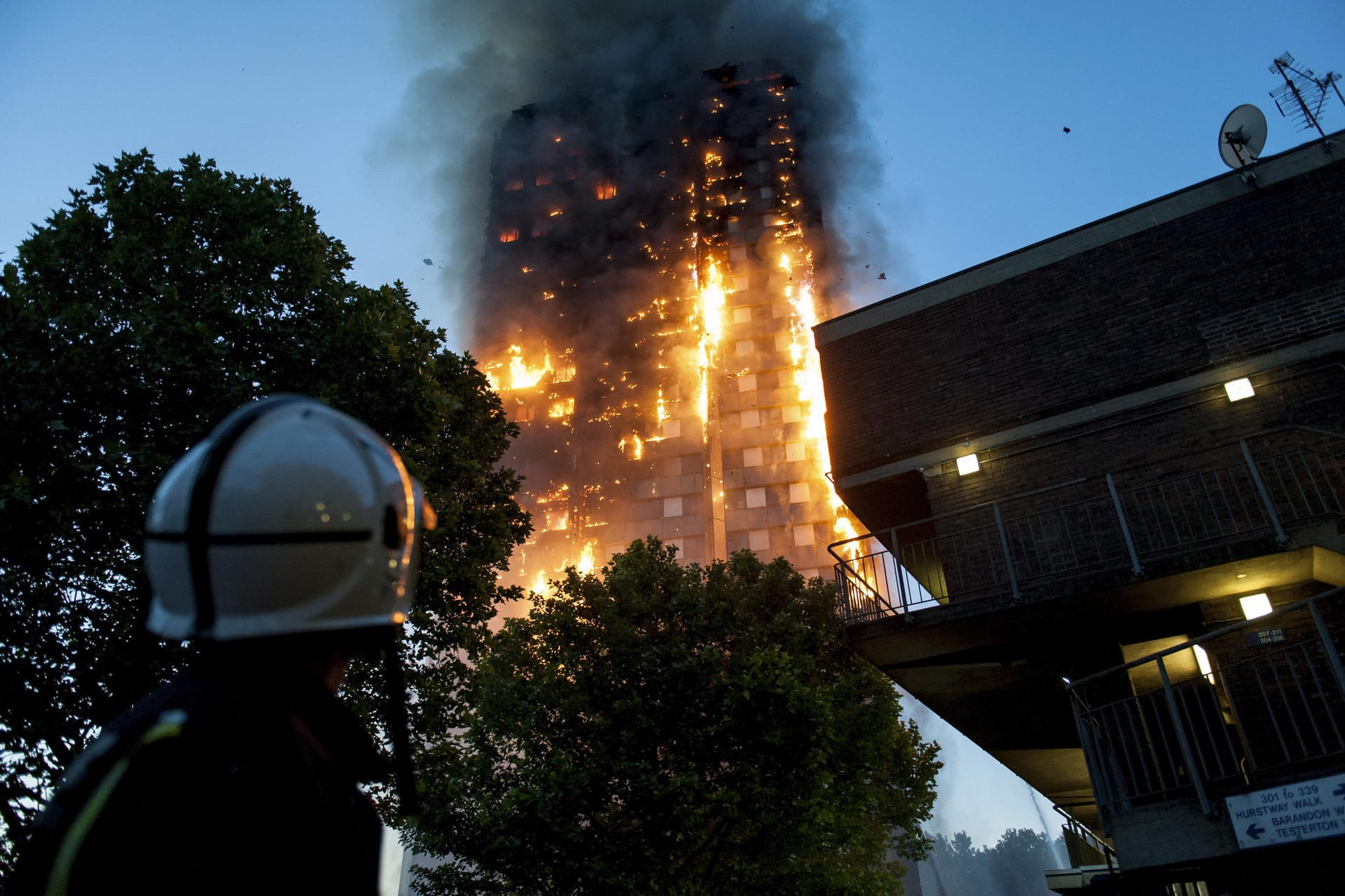 Feuerwehrleute beobachten hilflos, wie der Grenfell Tower in London abbrennt. Der Hochhausbrand steht beispielhaft für die Folgen von Sparwut und mangelhafte gesetzliche Vorschriften.