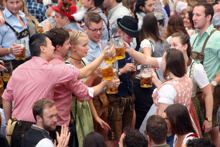 Auf dem Oktoberfest stoßen ausgelassen feiernde, junge Leute gemeinsam mit einer Maß Bier an.