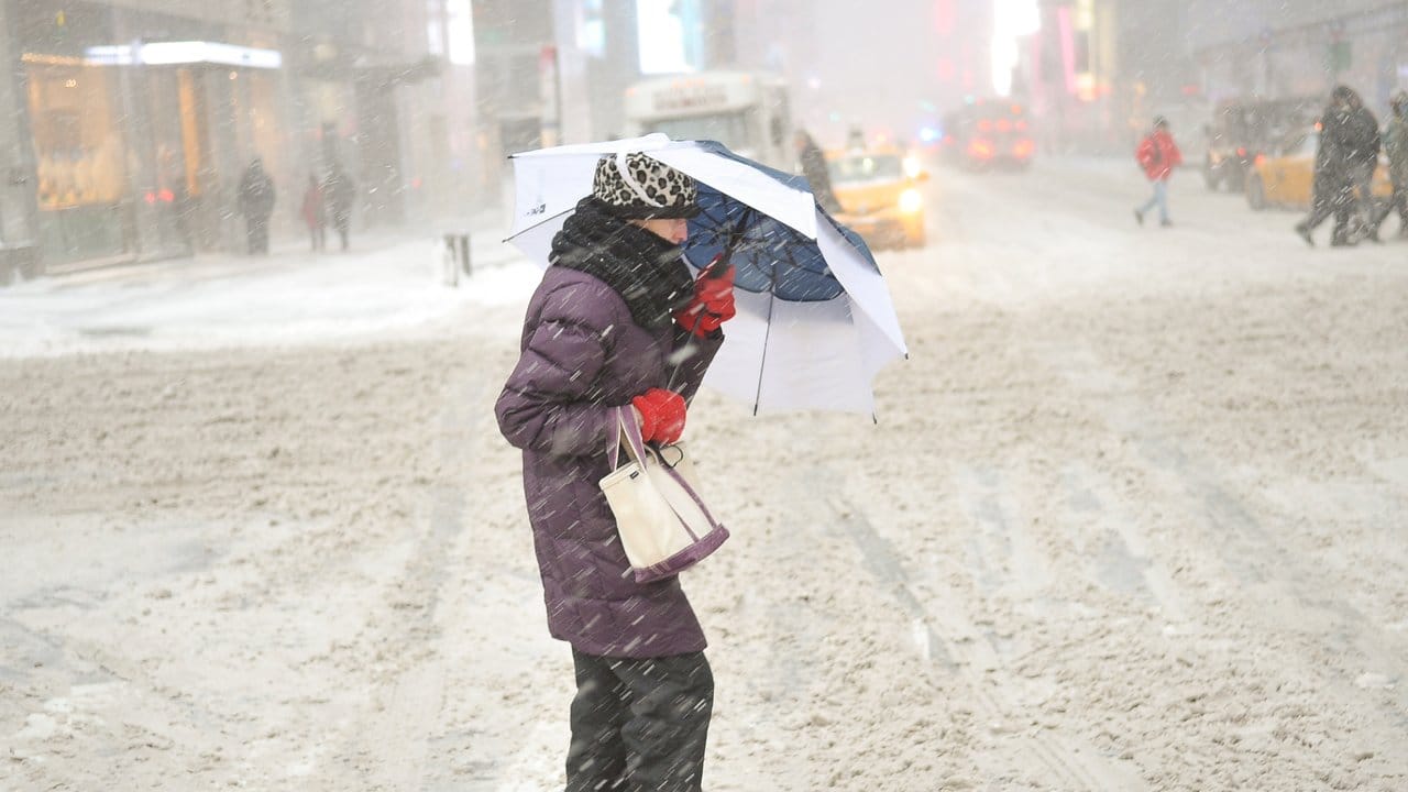Eine Frau versucht sich in New York mit einem Regenschirm vor Schnee und Wind zu schützen. Eine Frau versucht sich in New York mit einem Regenschirm vor Schnee und Wind zu schützen.