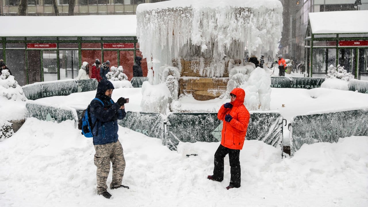 Ein Mann macht vor dem vereisten und verschneiten Bryant Park Brunnen in New York ein Foto. Ein Mann macht vor dem vereisten und verschneiten Bryant Park Brunnen in New York ein Foto.