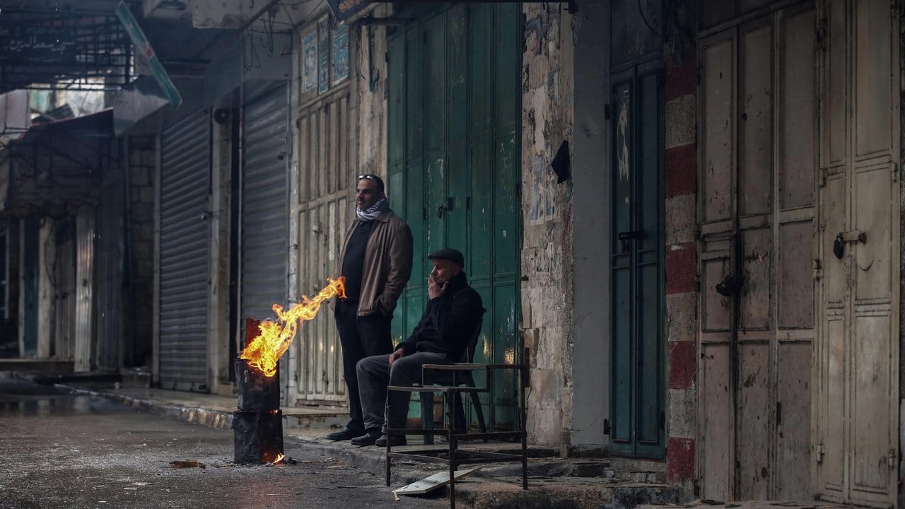 Zwei Männer wärmen sich an einem Feuer in der sonst leeren Straße eines Marktes in Nablus. Zwei Männer wärmen sich an einem Feuer in der sonst leeren Straße eines Marktes in Nablus.