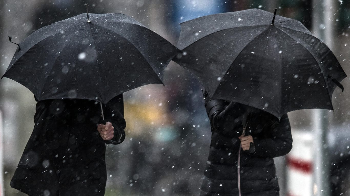 Fußgänger schützen sich in Düsseldorf (Nordrhein-Westfalen) mit Regenschirmen gegen den Schneeregen: Am Wochenende soll es Schnee und Regen geben, liegen bleibt der Schnee aber nicht.