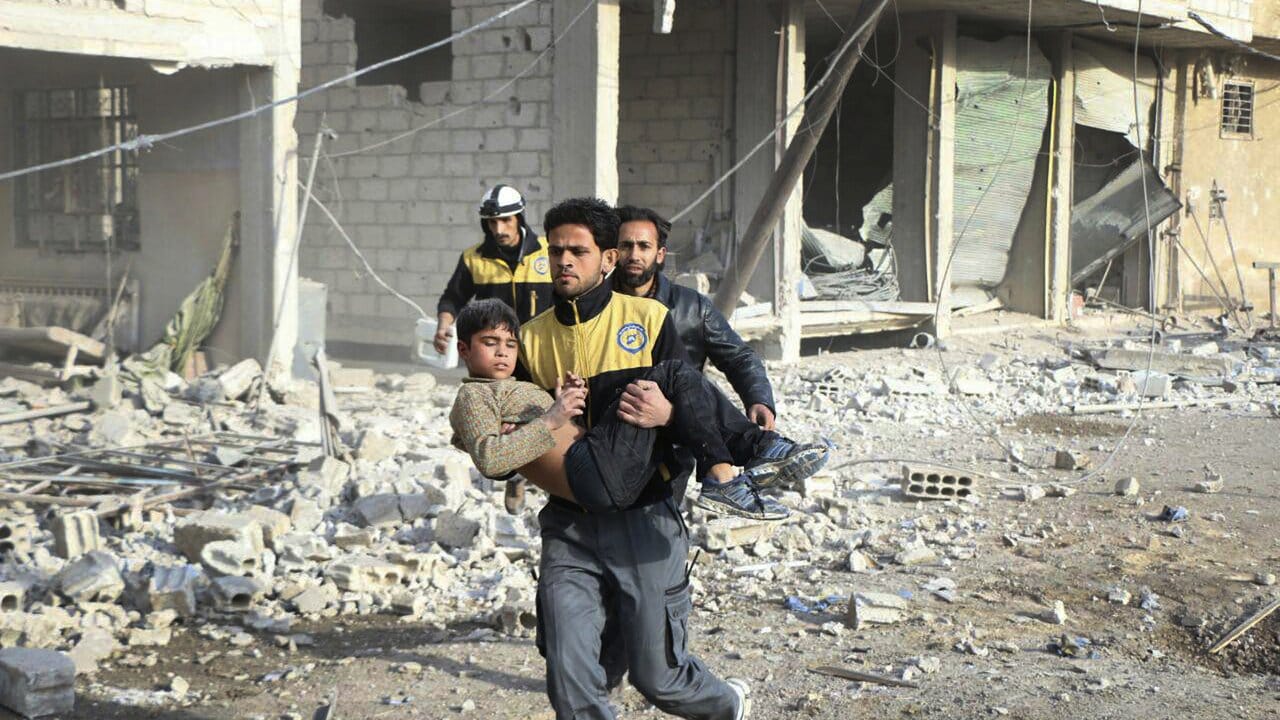 Mitglieder des syrischen Zivilschutzes ("Weißhelme") bergen während Luftangriffen einen verletzten Jungen. Mitglieder des syrischen Zivilschutzes ("Weißhelme") bergen während Luftangriffen einen verletzten Jungen.