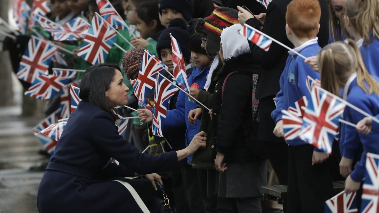 Auf Augenhöhe: Meghan Markle geht vor den Kindern mit den Union Jacks in die Hocke.