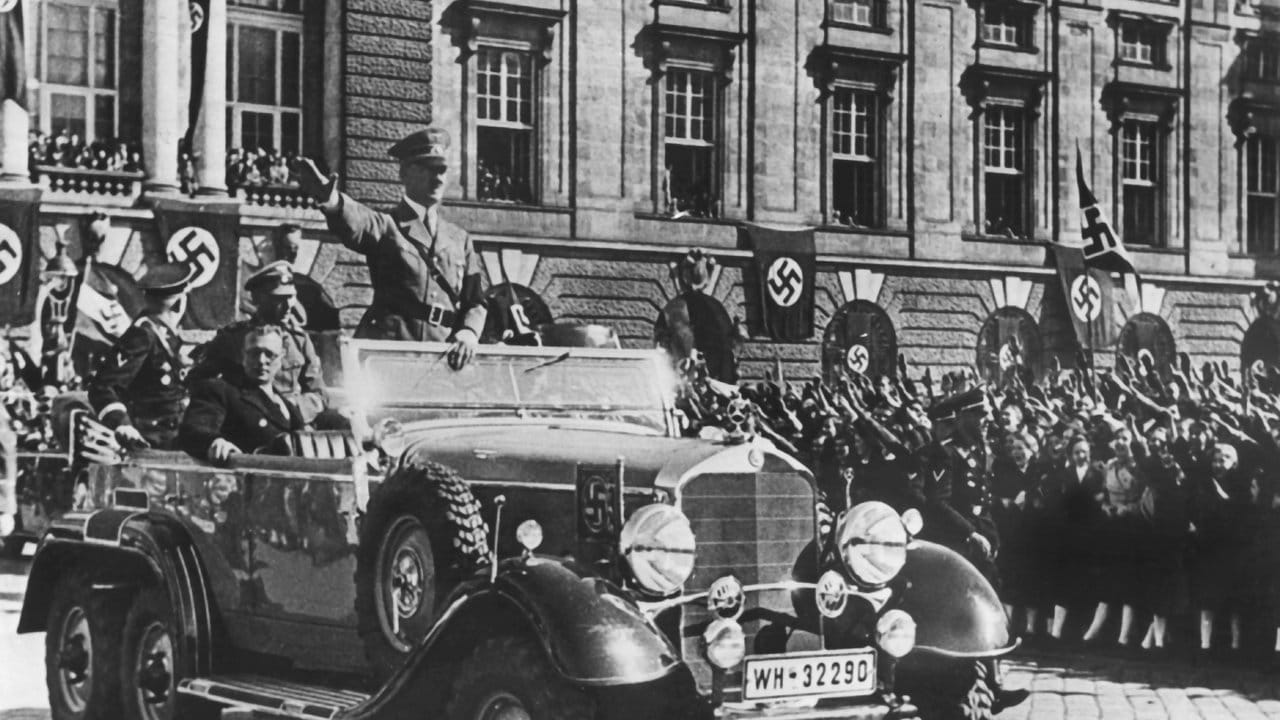 Adolf Hitler grüßt die ihm zujubelnde Menschenmenge in Wien, neben ihm sitzt der österreichische Kanzler Arthur Seyss-Inquart.