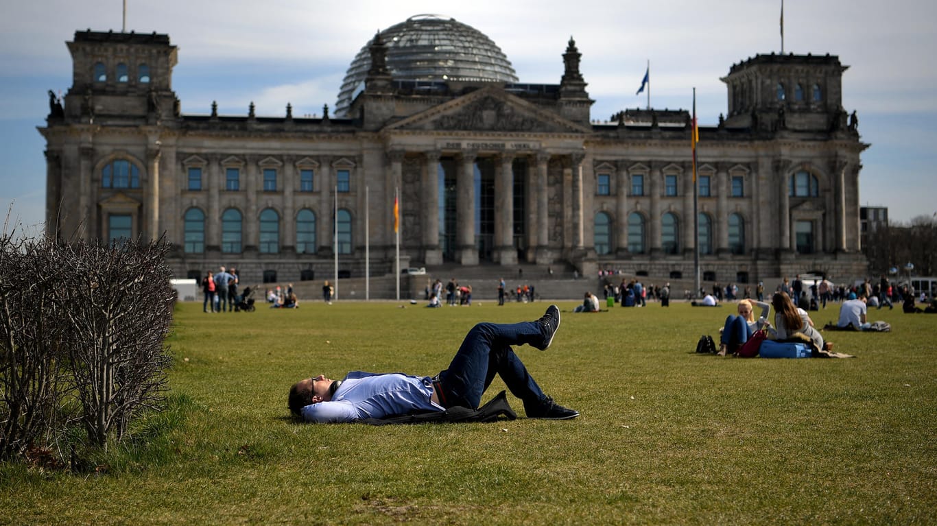 Menschen genießen die Sonnenstrahlen vor dem Reichstag in Berlin. In der Hauptstadt wird es die kommenden Tage sommerlich.