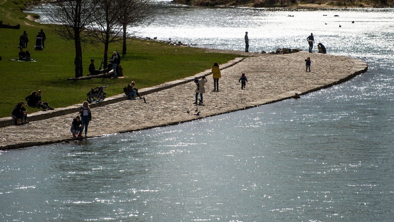 Personen sitzen bei blauem Himmel und Sonnenschein am Ufer der Isar. Personen sitzen bei blauem Himmel und Sonnenschein am Ufer der Isar.