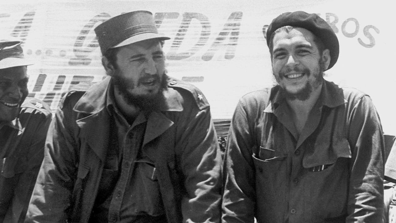 Fidel Castro (l), damals Ministerpräsident von Kuba, und der legendäre Guerilla-Führer Ernesto "Che" Guevara sehen auf einem Fliegerstützpunkt im August 1960 einer Bauern-Militärparade zu.
