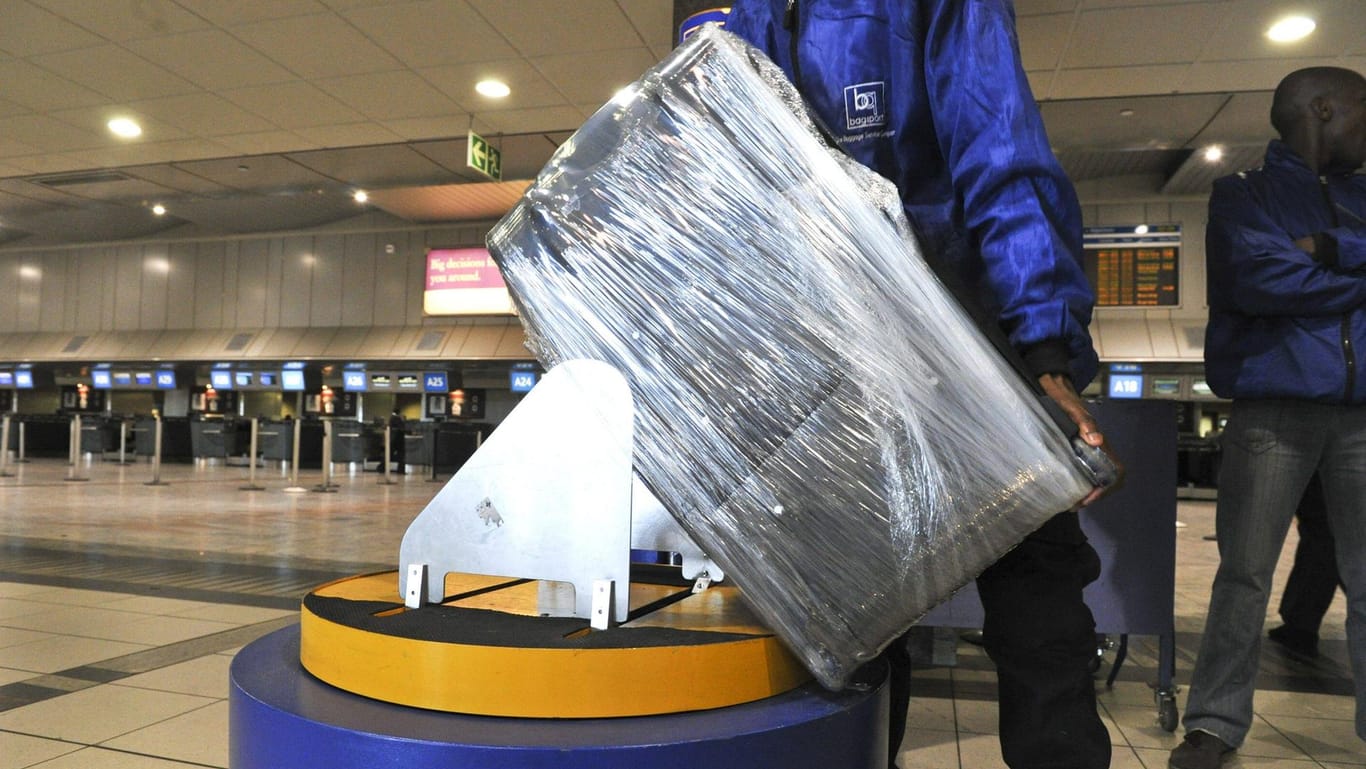 Vorsichtsmaßnahme und Schmutzschutz: Ein Flughafen-Angestellter wickelt einen Koffer in Folie.