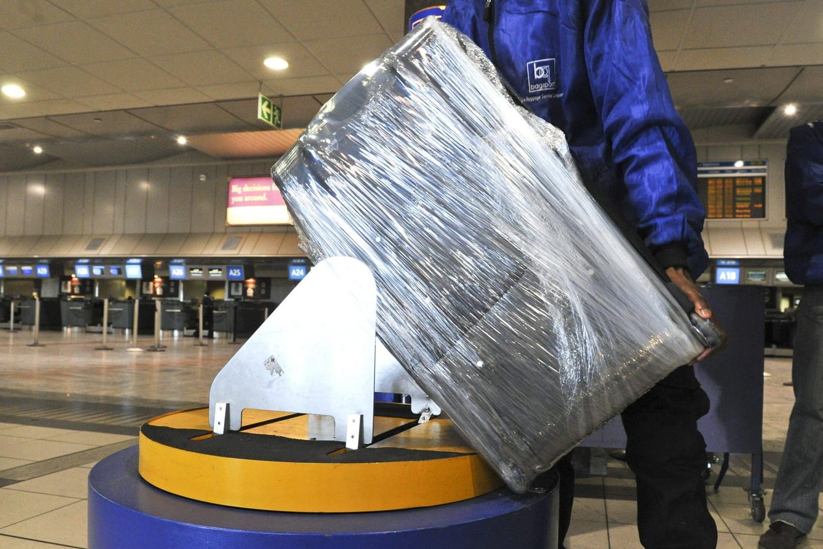 Vorsichtsmaßnahme und Schmutzschutz: Ein Flughafen-Angestellter wickelt einen Koffer in Folie.