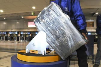 Vorsichtsmaßnahme und Schmutzschutz: Ein Flughafen-Angestellter wickelt einen Koffer in Folie.