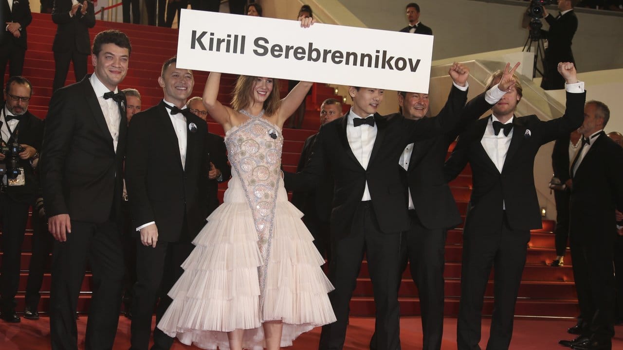 Die Schauspielerin Irina Starshenbaum (M) hält ein Schild mit dem Namen des in Russland unter Hausarrest stehenden Theatermachers Kirill Serebrennikow, während sie mit Produzent Charles-Evrard Tchekhoff (l-r), Schauspieler Roma Zver, Teo Yoo, Kameramann Vladislav Opelyants und Produzent Ilya Stewart zur Filmpremiere "Leto" über den roten Teppich läuft. Die Schauspielerin Irina Starshenbaum (M) hält ein Schild mit dem Namen des in Russland unter Hausarrest stehenden Theatermachers Kirill Serebrennikow, während sie mit Produzent Charles-Evrard Tchekhoff (l-r), Schauspieler Roma Zver, Teo Yoo, Kameramann Vladislav Opelyants und Produzent Ilya Stewart zur Filmpremiere "Leto" über den roten Teppich läuft.