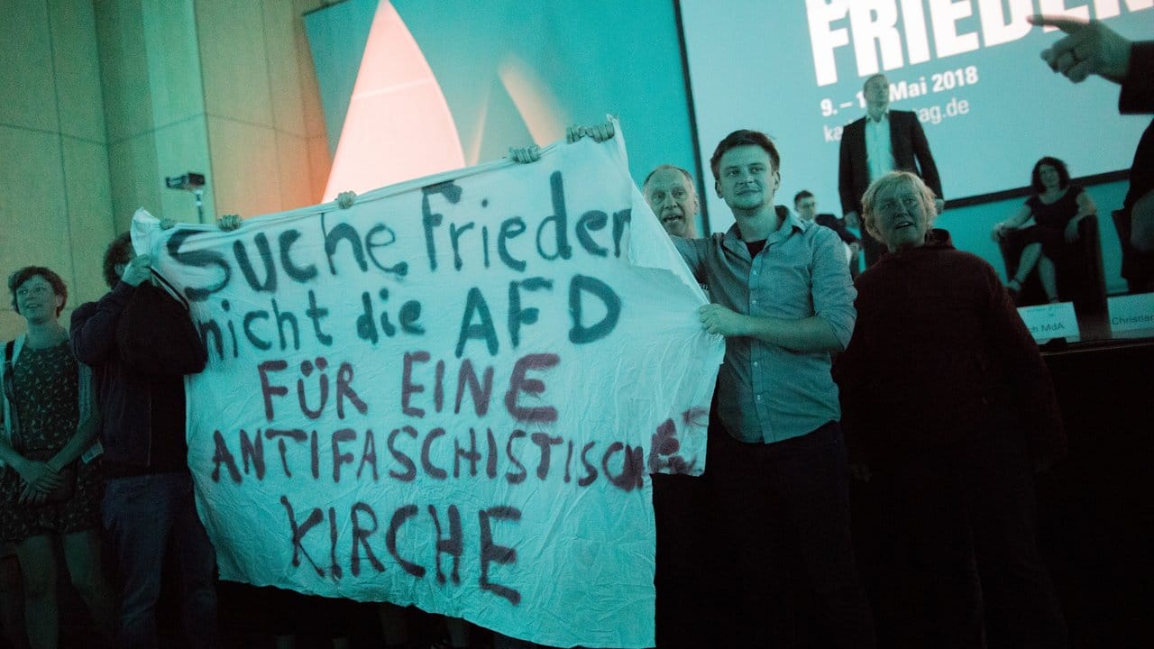 "Suche Frieden - nicht die AfD - für eine antifaschistische Kirche": Aktivisten halten vor der Bühne einer Podiumsdiskussion, an der AfD-Politiker Volker Münz teilnahm, ein Plakat hoch. "Suche Frieden - nicht die AfD - für eine antifaschistische Kirche": Aktivisten halten vor der Bühne einer Podiumsdiskussion, an der AfD-Politiker Volker Münz teilnahm, ein Plakat hoch.