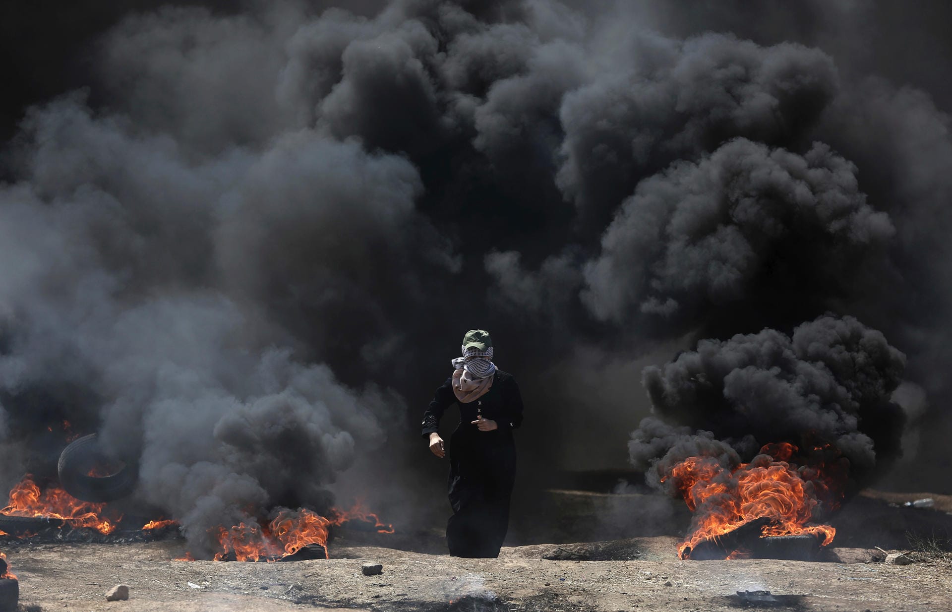 Eine palästinensische Frau läuft durch den schwarzen Rauch der brennenden Autoreifen.