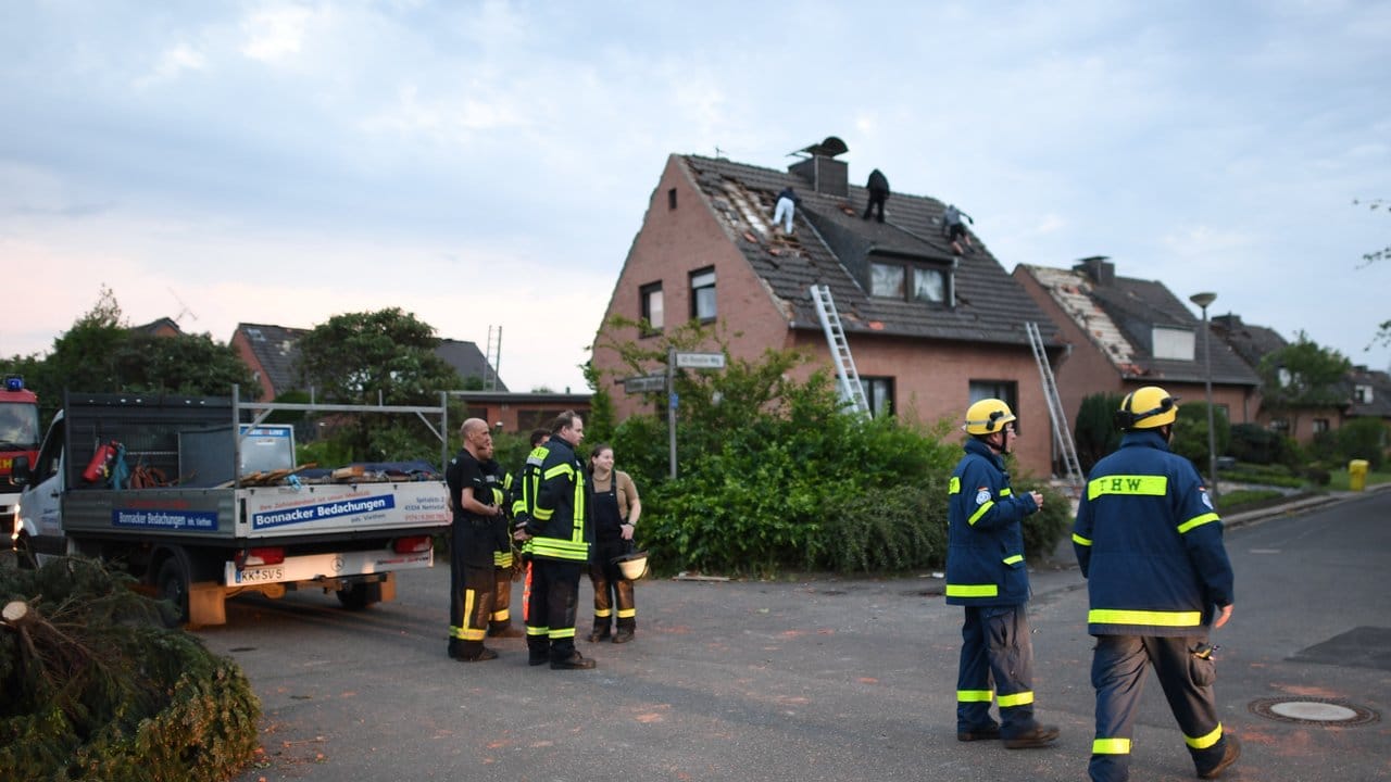 Einsatzkräfte der Feuerwehr und des THW stehen neben Häusern, die von einem Wirbelsturm beschädigt wurden.