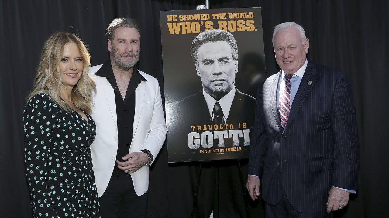 John Travolta, seine Frau Kelly Preston (l) und Marty Golden (r), Mitglied des Senats des Bundesstaats New York, neben einem Poster zu Travoltas neuem Film "Gotti" in Brooklyn.