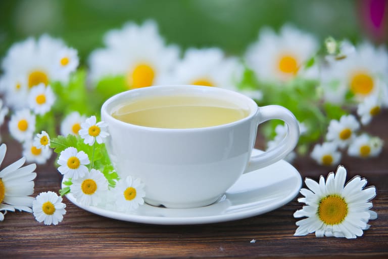 Tasse Tee mit Kamillen im Hintergrund