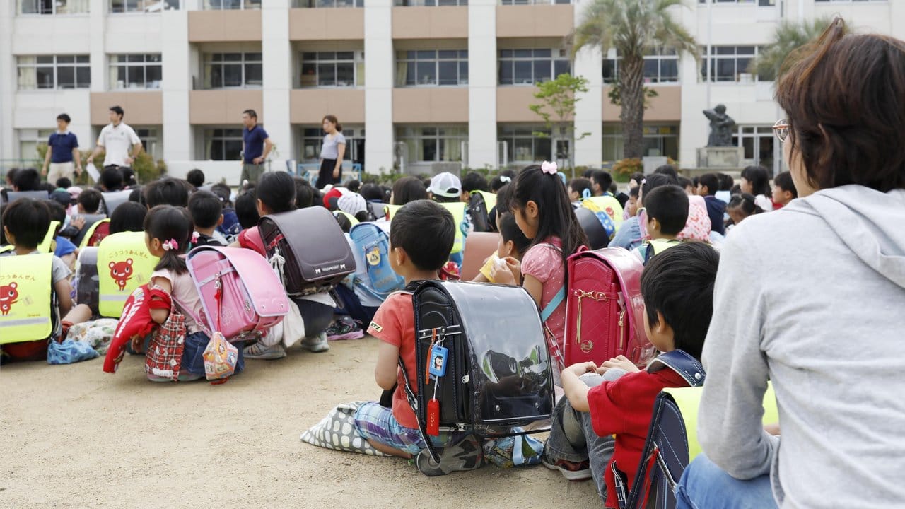 Schüler sitzen nach der Evakuierung ihrer Grundschule in Ikeda auf dem Schulhof.