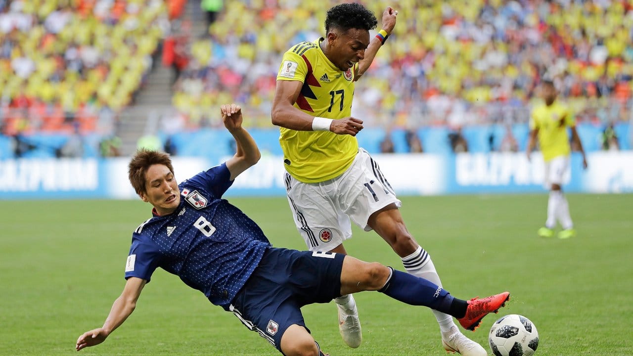 Japans Genki Haraguchi (l) grätscht gegen Kolumbiens Johan Mojica um an den Ball zu kommen.