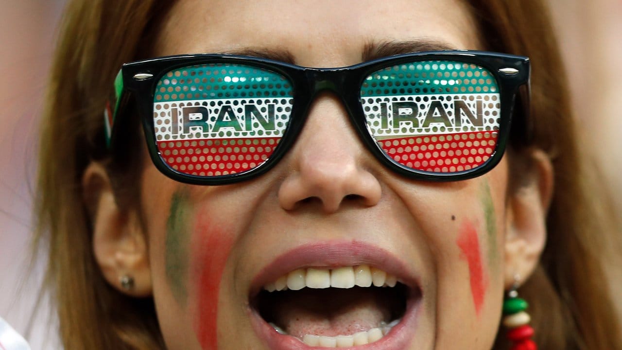 Ein weiblicher iranischer Fan steht vor Spielbeginn mit einer Brille mit dem Schriftzug "Iran" im Stadion.