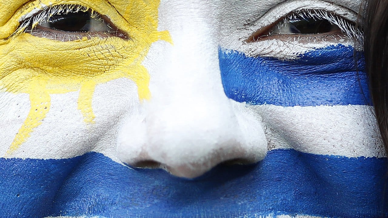 Ein Fan der Nationalmannschaft von Uruguay lächelt mit der Flagge von Uruguay als Gesichtsbemalung.