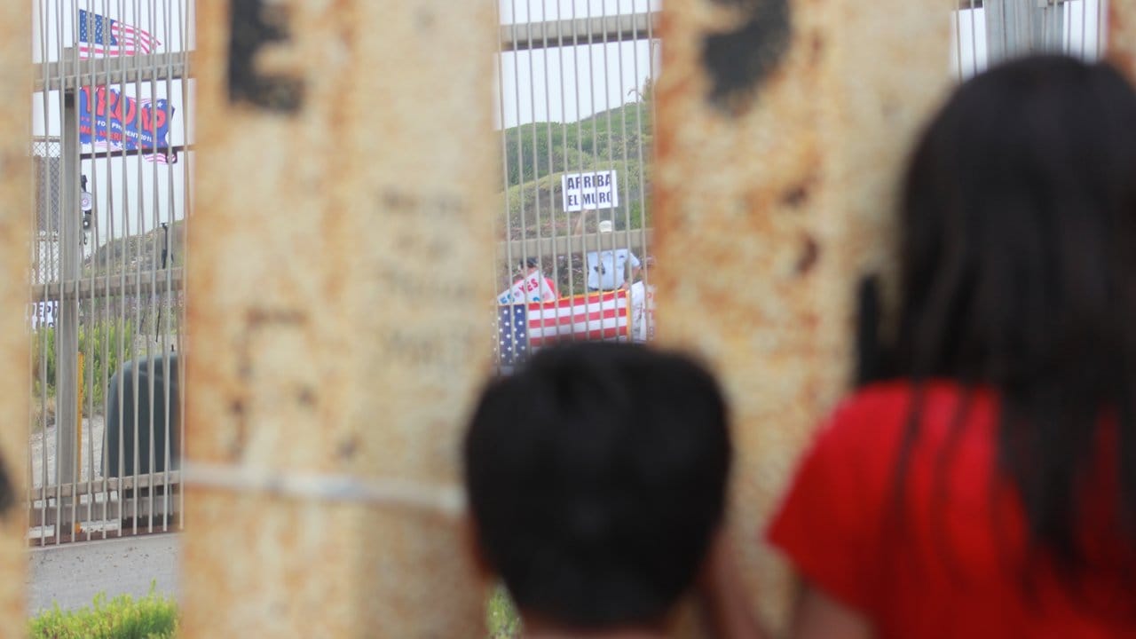 Blick nach drüben: Mexikanische Kinder beobachten durch den Grenzzaun Trump-Anhänger, die eine Verstärkung der Mauer fordern. Blick nach drüben: Mexikanische Kinder beobachten durch den Grenzzaun Trump-Anhänger, die eine Verstärkung der Mauer fordern.
