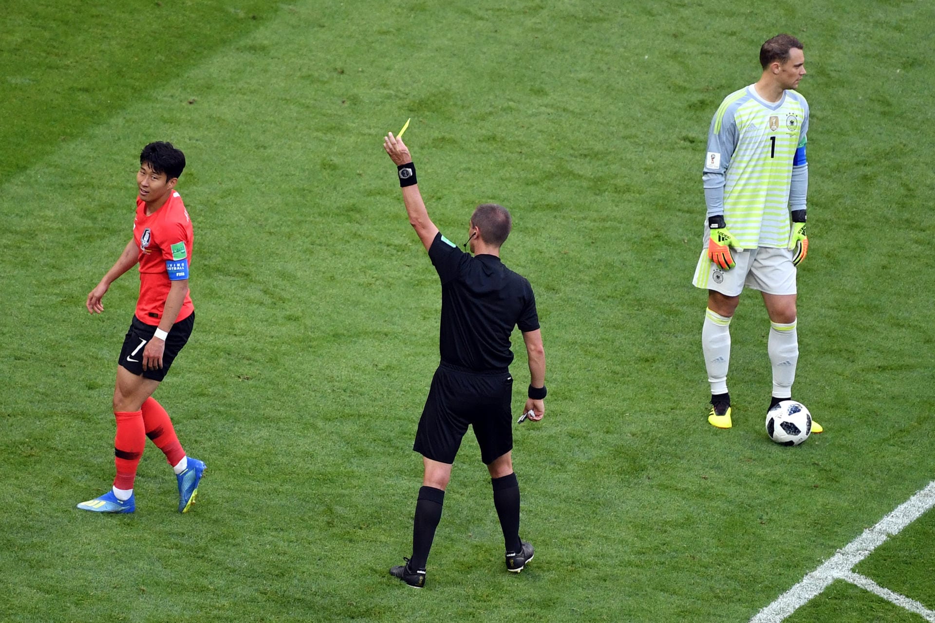 Schiedsrichter Mark Geiger aus den USA (M) zeigt Heungmin Son (l) die gelbe Karte neben Torwart Manuel Neuer.
