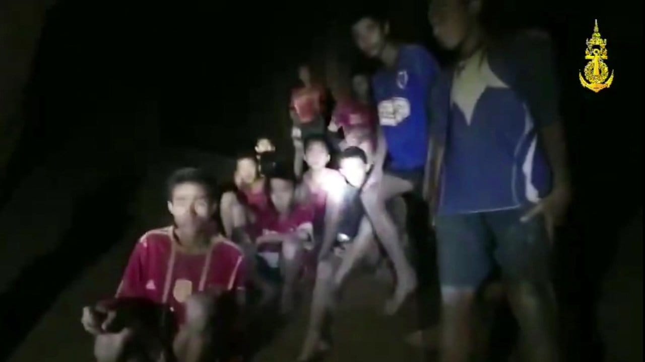 Ein Video-Standbild einer thailändischen Spezialeinheit zeigt die vermissten Jugendfußballer und ihren Trainer, nachdem sie in einer Höhle entdeckt wurden. Ein Video-Standbild einer thailändischen Spezialeinheit zeigt die vermissten Jugendfußballer und ihren Trainer, nachdem sie in einer Höhle entdeckt wurden.