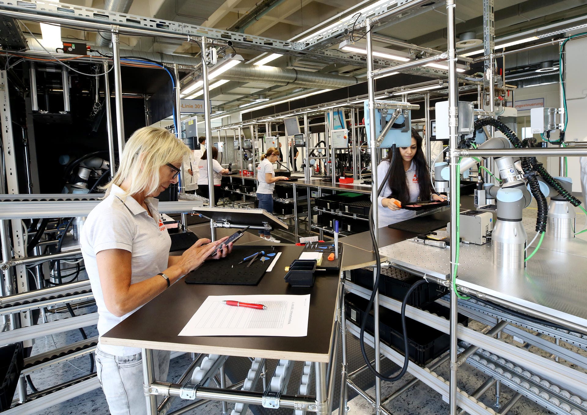 Mitarbeiterinnen und Roboter montieren die Smartphones in der Gigaset-Firma im Münsterland.