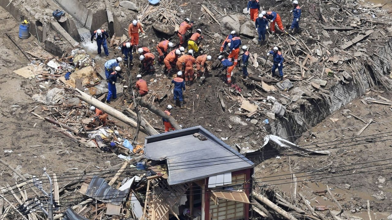 Kitakyushu: Blick auf Einsatzkräfte, die nach Vermissten suchen und Wohnhäuser, die durch eine Schlammlawine zerstört wurden.