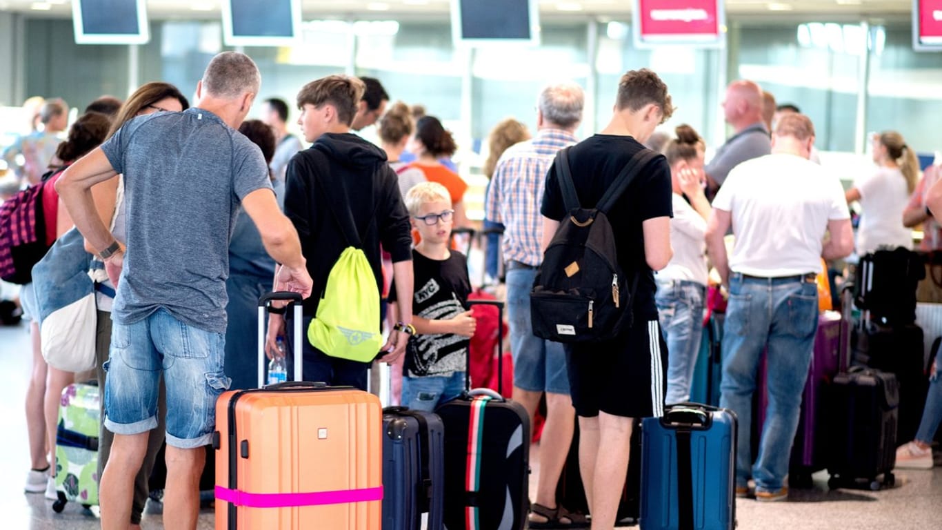 Fluggäste stehen mit ihrem Gepäck vor einem Check-in-Schalter in der Abflughalle des Flughafens Hannover.