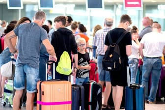 Fluggäste stehen mit ihrem Gepäck vor einem Check-in-Schalter in der Abflughalle des Flughafens Hannover.