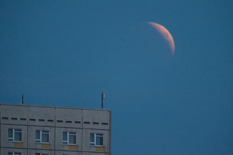 Die Mondfinsternis beginnt: Der aufgehende Mond ist hinter einem Hotelgebäude in Dresden zu sehen.